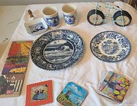 Overall lot layout showing plates, mugs, bicycle coaster holder, coasters, card decks