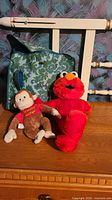 Elmo and Curious George plush toys in front of green floral bag