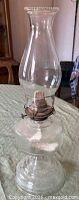 Full view of clear glass oil lamp showing chimney, burner, reservoir and base
