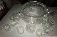 Clear pressed-glass punch bowl with pattern, four cups hanging from hooks, additional cups arranged around bowl