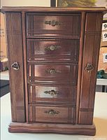 Front view of closed wooden jewelry box showing drawers and side doors