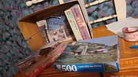 Overview of open box and two puzzles in front showing farmland 500-piece box, Canada 3000 box, Star and Royal puzzles inside