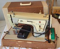 Complete Singer sewing machine mounted in base with foot pedal and accessory tray, case lid behind