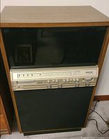 Front view of closed stereo console showing cabinet and control panel behind smoked glass