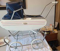 Full view of white metal doll stroller with navy vinyl hood and chrome frame
