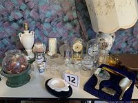 overview of tabletop showing lamp, vanity set, glass dome clocks, glassware, ceramics