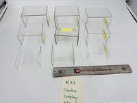 Nine clear acrylic display risers of varying sizes with ruler for scale
