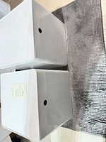 two white plastic IKEA storage cubes with lids, front view showing handle openings