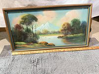 Full view of framed mountain landscape painting with ruler for scale