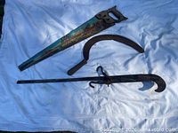 Overall view of hand saw, sickle and hook laid on cloth
