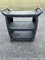 Front view of three-tier black plastic cart showing shelves and handles