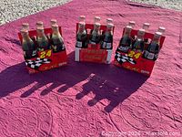 Three full 6-pack carriers of sealed Coca-Cola bottles on mat