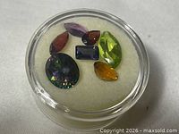 Top view of all seven loose gemstones inside round plastic case