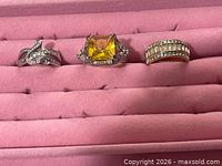 Three rings arranged in a jewelry tray: crossover, yellow topaz cocktail, eternity band