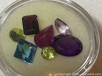 Seven gemstones in round display case showing colours and shapes