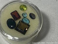 Top view of seven gemstones in display case showing colors and cuts