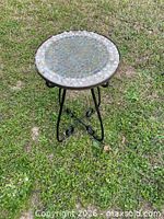 full view of round mosaic top and metal base on grass