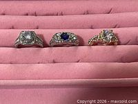 Front view of three rings in pink tray showing metals, center stones and halos