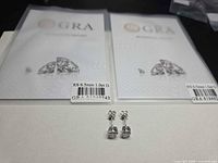 Earrings with two GRA report cards showing 6.5mm 1.0ct D data