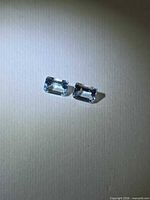 Both emerald-cut aquamarines side by side on neutral background