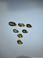 Seven loose green-champagne tanzanite stones arranged on white background