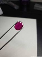 Oval blood red ruby held by tweezers showing crown facets