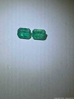 Pair of rectangular emerald-cut emeralds on neutral background