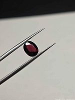 Front view of red oval spinel held in tweezers