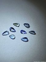 Eight small pear-cut tanzanite stones on neutral background