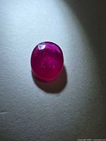 Oval blood-red ruby on neutral background showing face-up view