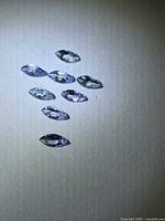 Eight small marquise-cut violet-blue gemstones on light surface