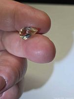 Pear-cut gemstone held between fingers showing yellow hue