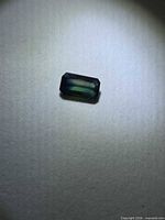 Loose emerald-cut blue-green sapphire on neutral background