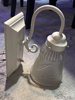 Front view of sconce showing metal backplate, arm and frosted glass shade