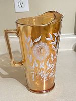 Left side of amber carnival glass pitcher showing handle, floral enamel, spout