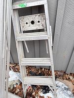 Full view of folded aluminum step ladder leaning against wall, showing three steps and tool tray