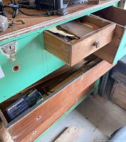 Open top drawer of green workbench showing sandpaper sheets and Mastercraft boxed accessory below