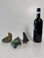 Group shot of three soapstone marine mammal figurines beside wine bottle for scale