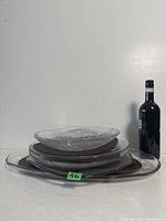 Stack of five large clear glass trays of various sizes with wine bottle for scale