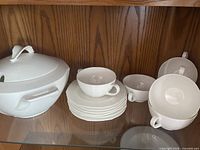 Covered soup tureen, stack of saucers, multiple cream soup cups on shelf