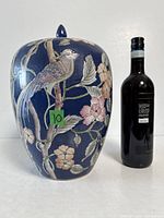 Front view of blue ginger jar with bird and floral decoration, lid on, bottle for scale