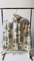 Full front view of ivory silk Christian Dior blouse with black print on hanger