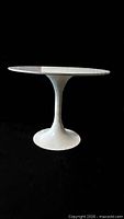 Full view of white tulip pedestal table against dark background