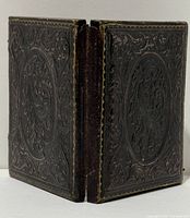 Closed embossed leather case showing foliate design and worn spine