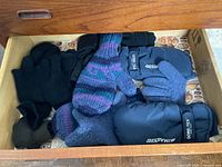 Open drawer showing multiple pairs of winter gloves in various materials and colours