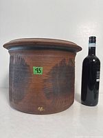 Full view of cylindrical stoneware vessel with lid beside wine bottle