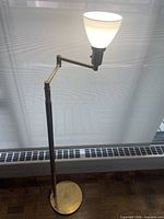 Full view of brass floor lamp, articulated arm extended, shade illuminated