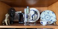 Shelf showing all decorative items including brass lion, wood bust, lacquered frame, glass vase, amphora, metal figure, and three pieces of blue-and-white porcelain