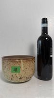 Front view of speckled stoneware bowl beside wine bottle for scale