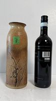 Front view of signed Vladimir Kravjansky stoneware vase next to wine bottle for scale